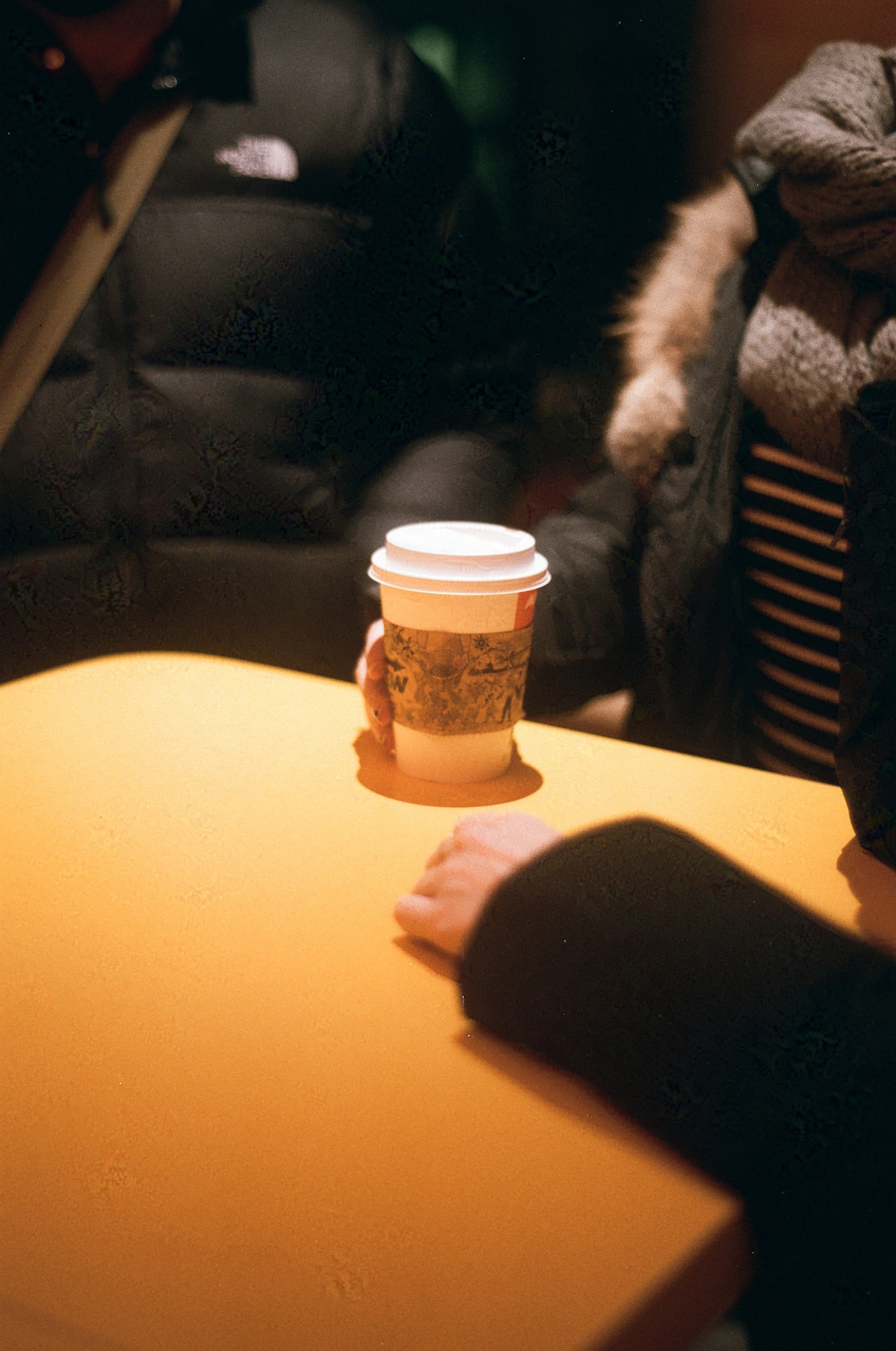 several people around an empty table, one of them holding a to-go cup of coffee