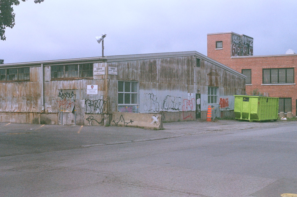 A weather-worn and graffitied warehouse & bright green garbage container