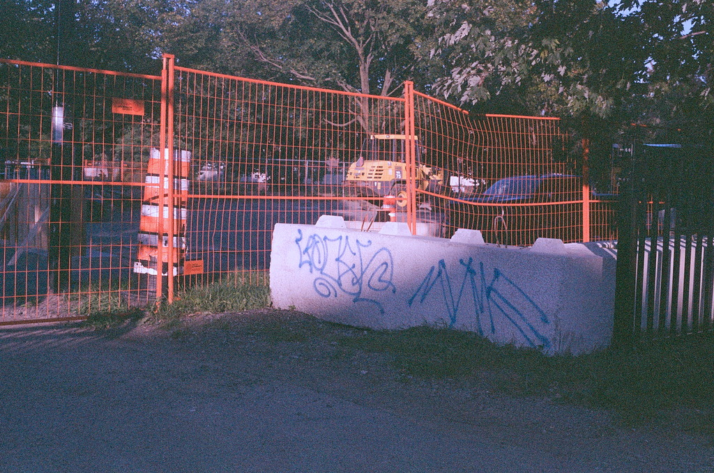 An orange temporary fence around a dig site and a cinder bollard