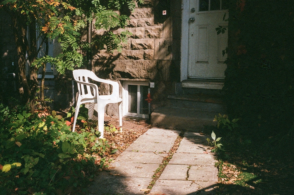 A plastic lawn chair under dramatic light in front of an apartment building