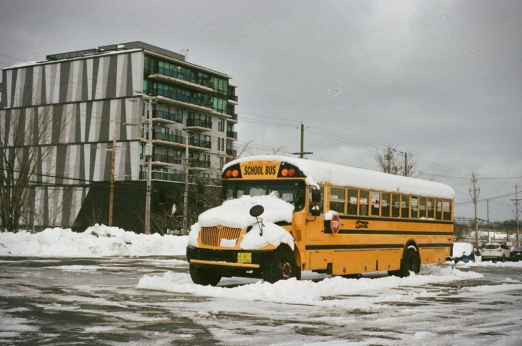 A yellow school bus in a parking lot, under snow