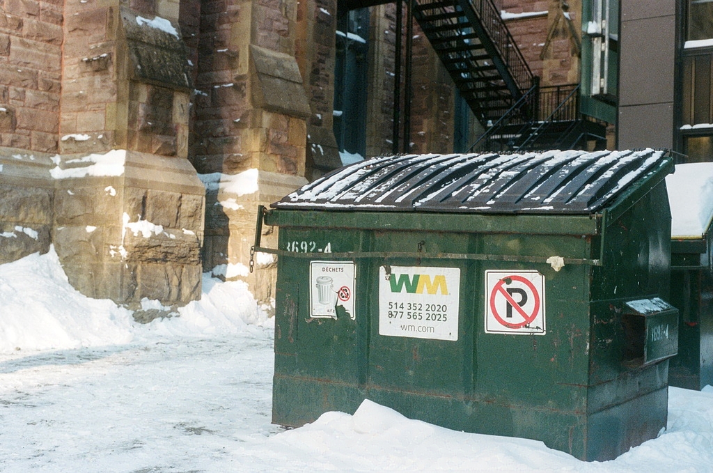 A green garbage bin in an alley by a church