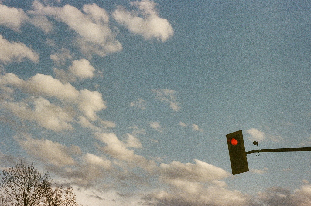 A red traffic light against a few tufts of cloud in the sky