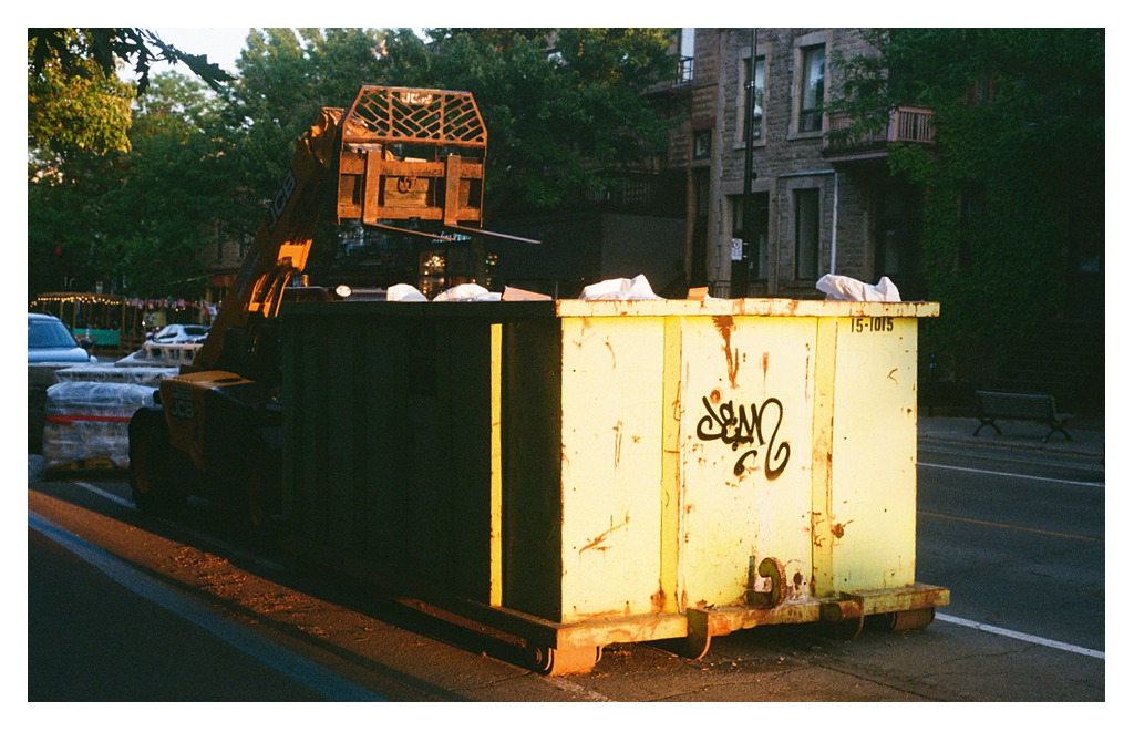 A construction dumpster and small forklift in dramatic evening light