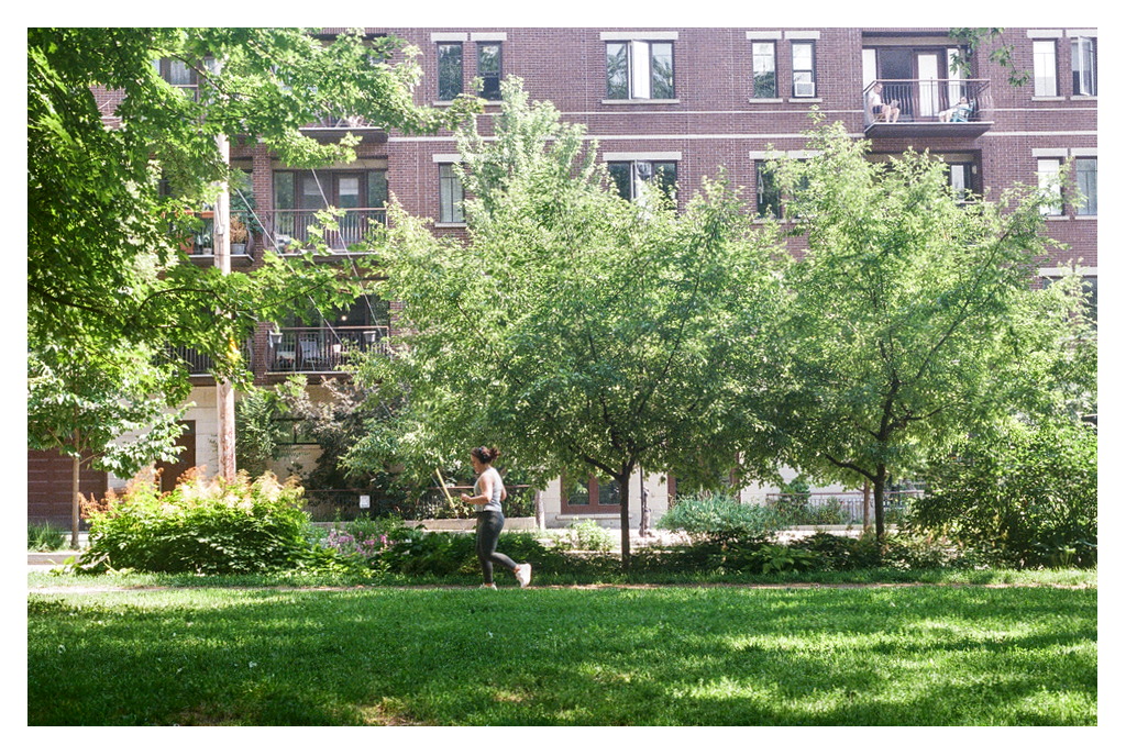 A person jogs in a park, with people on balconies behind