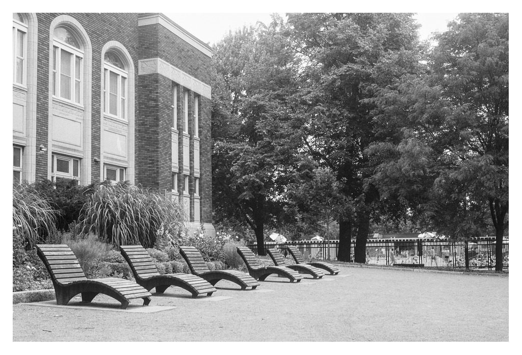 Sun tanning benches in the park, with a pool in the background (B&W version)