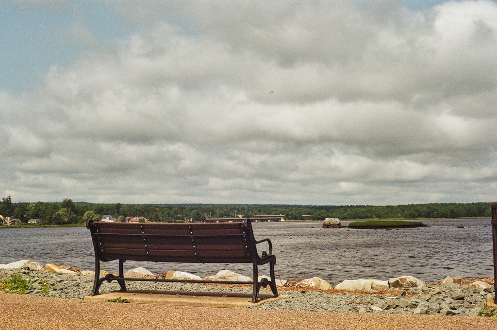 An empty park bench looking out over a lake with short waves