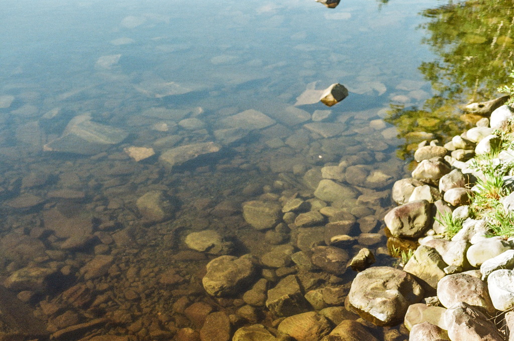 Rocks above and below water by a clear pond