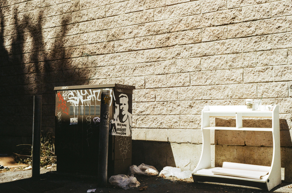 A transformer box with a stencil of Robert Paulson, and some alley trash
