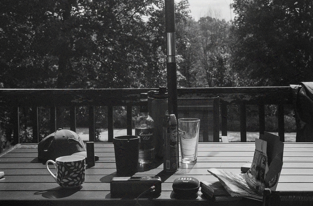 A table covered with various outdoor gear: a speaker, mugs & glasses, a hat