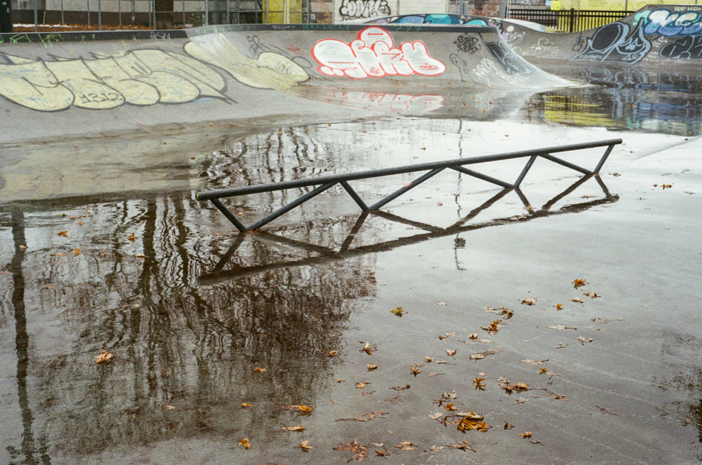 A skateboard railing in a concrete skate park, reflective with rain