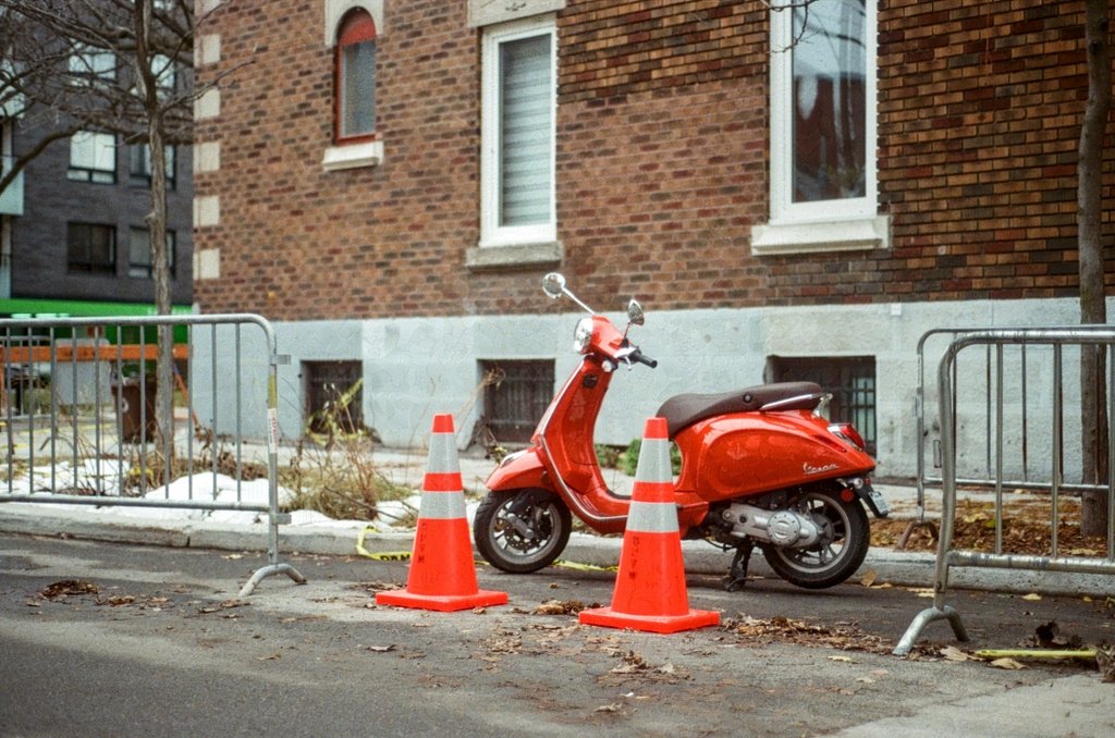 A red scooter behind traffic cones by the side of the road