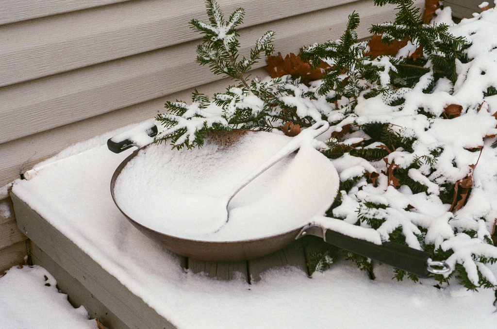 A wok and some pine boughs on a balcony, under a layer of snow
