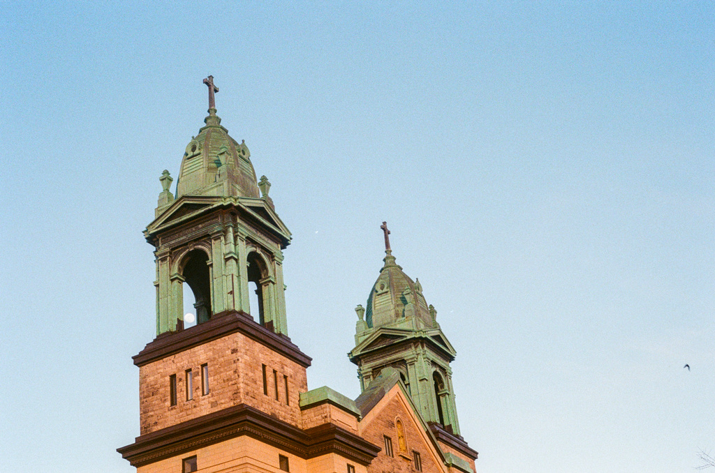 Two church spires reach up in the dusk light; the near-full moon shows through one of the bell towers