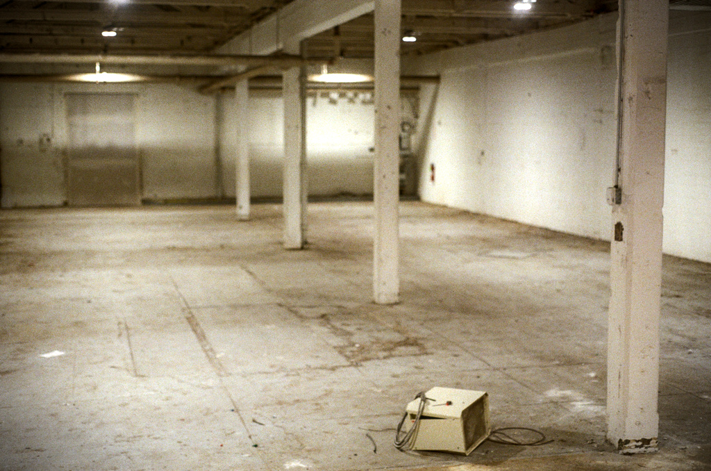 A grey, empty warehouse, with a discarded appliance on the floor