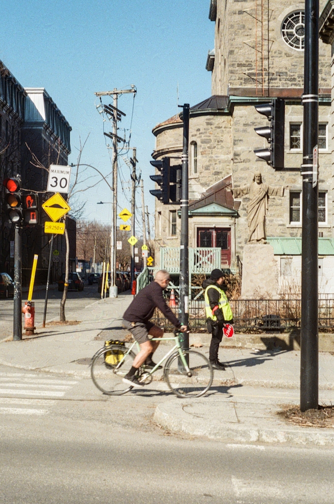 A cyclist speeds by a crossing guard on Rachel & Henri-Julien