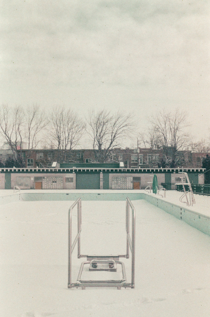 The railings of a diving board, with no board, over Laurier pool, which is filled with snow