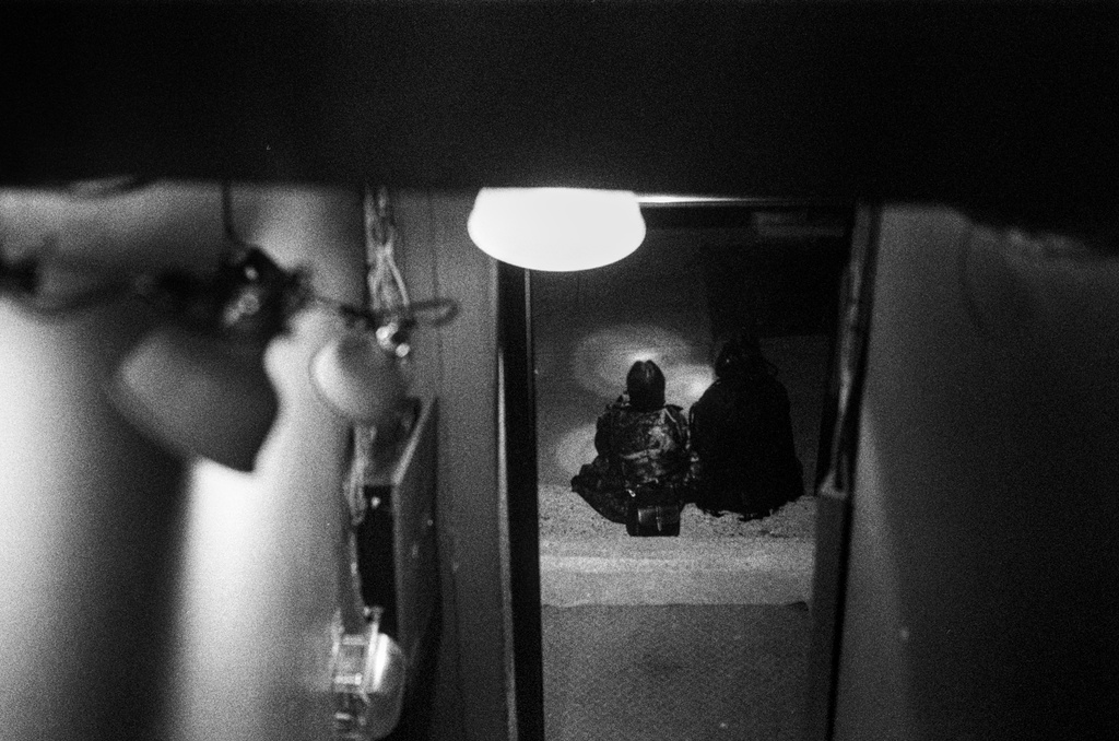 Two people sit on the sidewalk outside of a bar at night