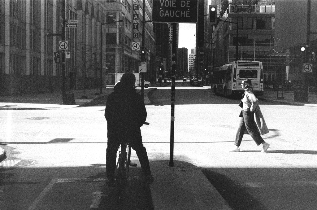 A cyclist stops at the median as a pedestrian crosses the street