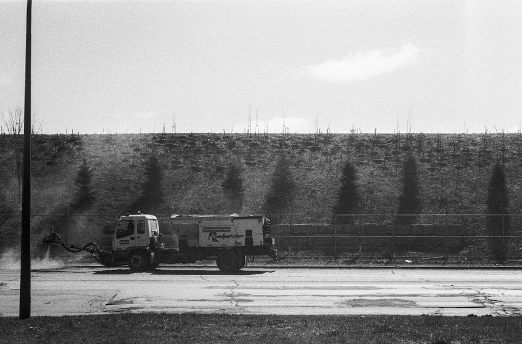 A small truck repatches the asphalt in front of an artificial hill