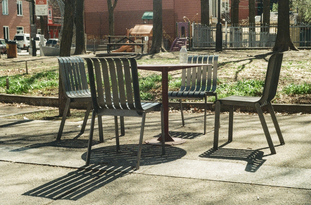 Four metal chairs around a metal park table, casting strong shadows