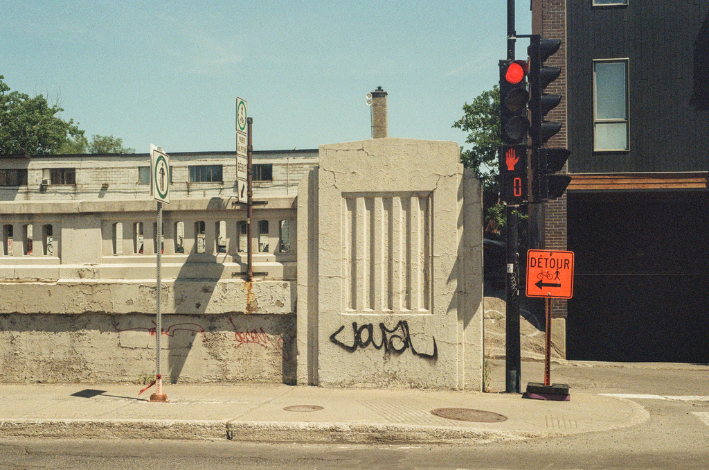 An orange detour sign on a sidewalk near an underpass