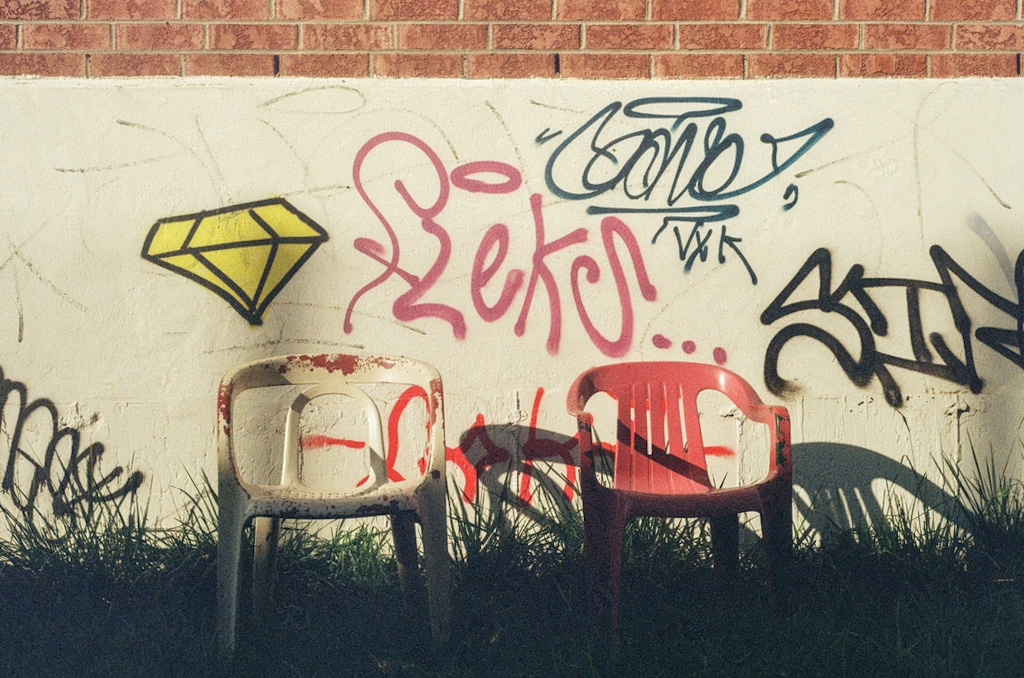 Two plastic chairs in front of a wall covered in graffiti
