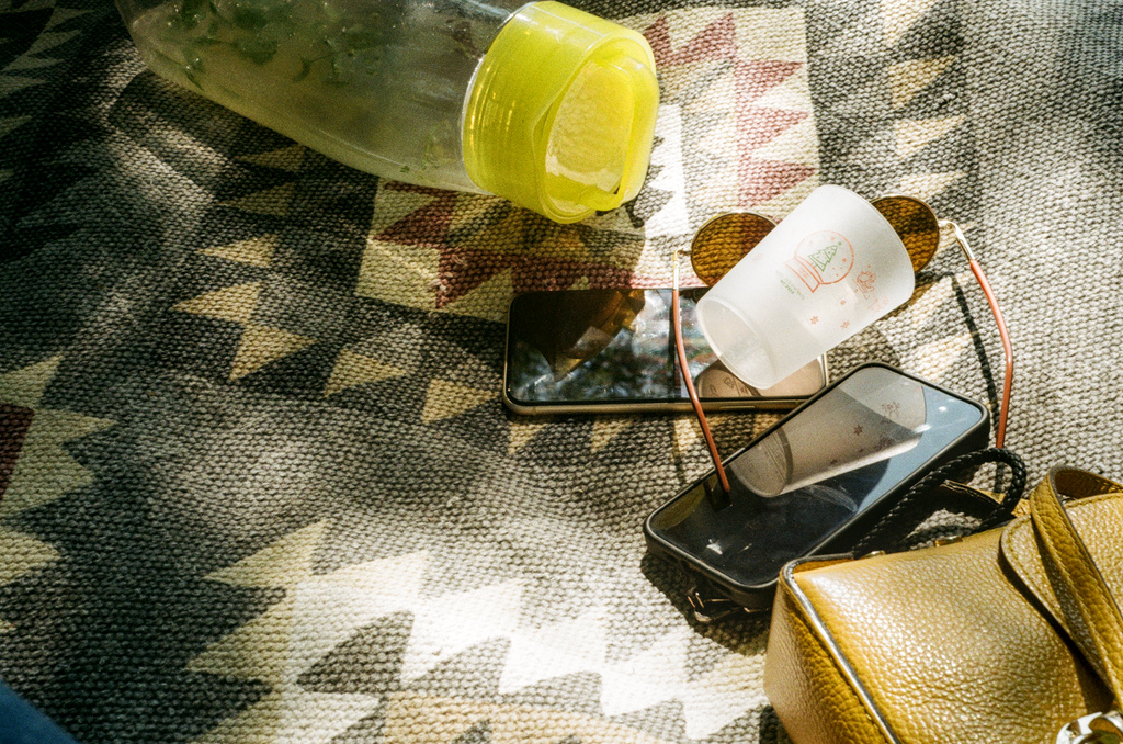 A picnic blanket with phones, sunglasses, a purse, and a water bottle