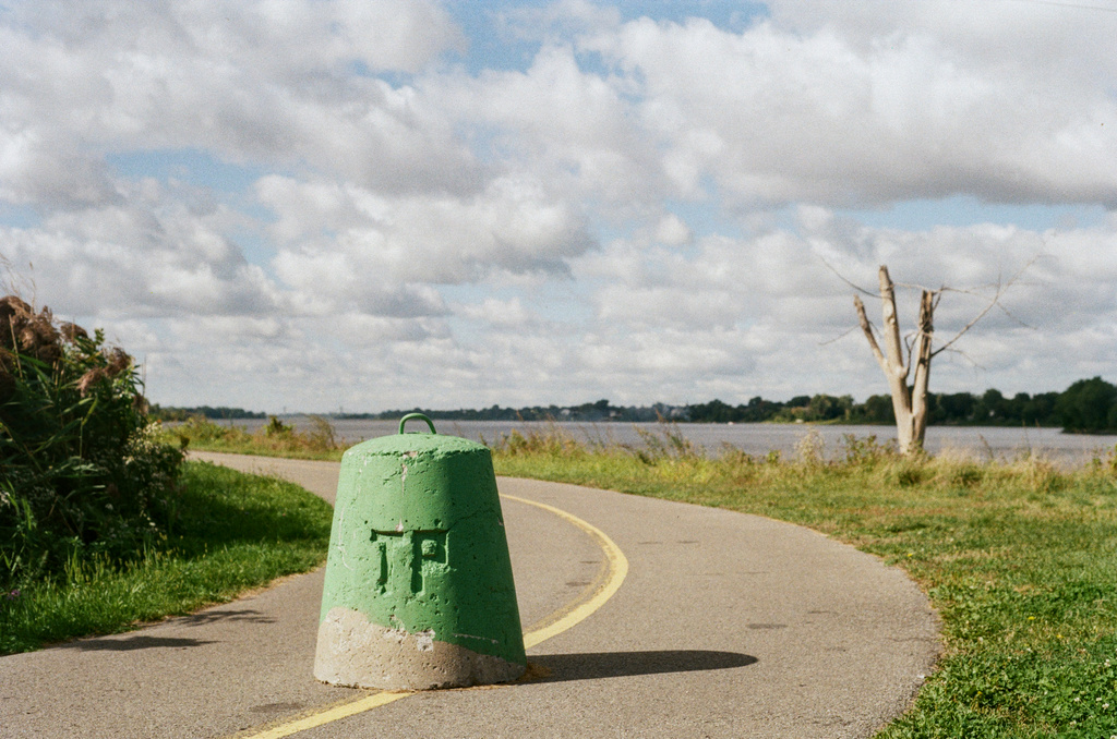 A green painted bollard, with a "TP" imprint, on a bike path