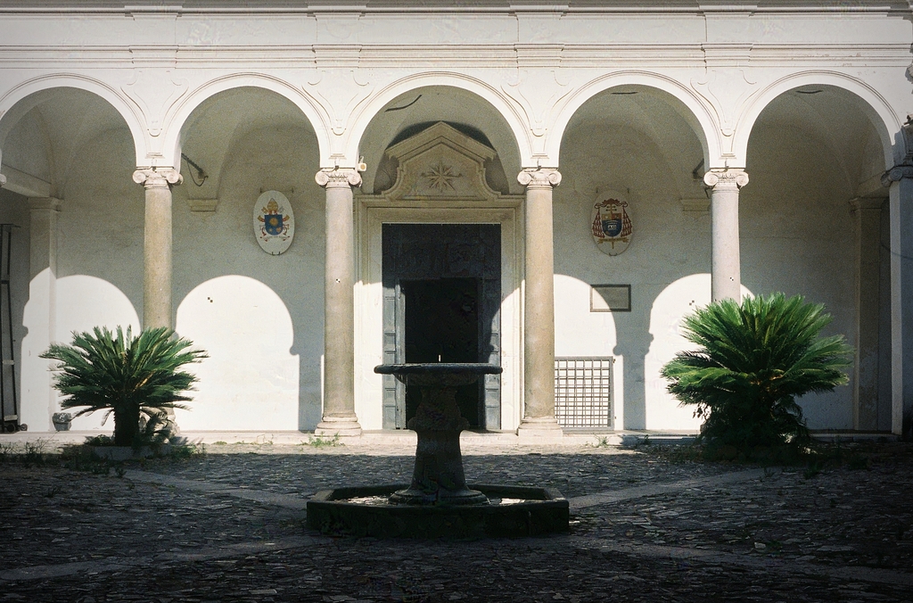 A courtyard with fountain at the Basilica di San Clemente, under harsh sunlight