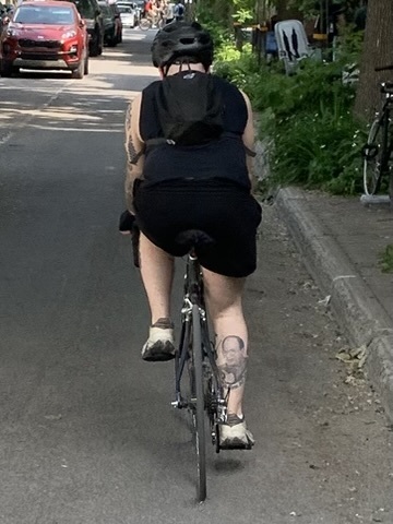Approaching a cyclist from behind; their calf has a tattoo of George Costanza