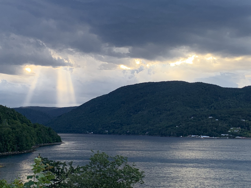 God rays breaking through dramatic clouds, over mountains and a lake